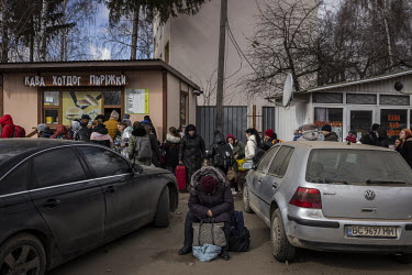 A woman rests as behind her a people wait to cross the border. A crowd of several thousand or more, mainly women and children, queue up in the freezing cold at the Shehyni border crossing between Ukra...