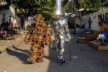 'L'homme miroir' by Patrick Kitete walking with The Coconut Man, who fights against deforestation, walking together in 'la vie est belle', an artists' cooperative in the Matonge district. It is a plac...
