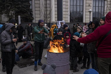 People warm themselves around a fire outside Lviv train station where thousands fleeing the war queued to board evacuation trains.