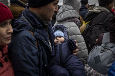 A man carries a baby wrapped up against the cold as a train full of passengers crowd onto a platform at Lviv train station after they arrived from Kiev (Kyiv).
