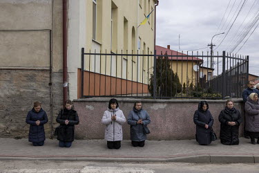 Local residents kneel on the pavement as the funeral procession for Senior Sergent Yevhen Verveyko of the Ukranian National Army, who was killed fighting against Russian forces, passes through the tow...