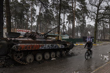 A man rides a bicycle past a destroyed Russian tank in the recently liberated town of Bucha.