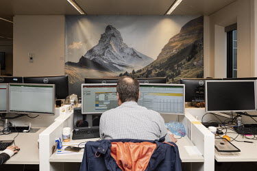 An employee at work in his office at the headquarters of Rabobank, with a canvas depicting the Matterhorn in Switzerland in the background.