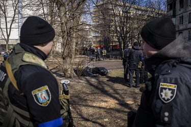 Police officers on guard near the bodies of two people who died after their building in western Kyiv was hit by Russian shelling and caught on fire.