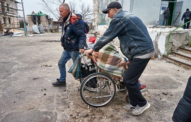 Men helping a woman in wheelchair during an evacuation from Rubizhne. People have been hiding in bomb shelters for several weeks, they gathered at the House of Culture where they have been waiting to...