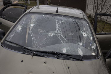 A bullet riddled civilian car, that has blood stains on the front and rear seats, lies on the side of a road in Bucha.