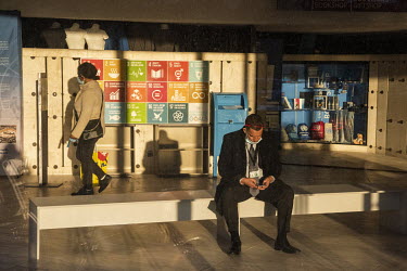 Dipomatic staff ('D') sitting on a bench in front of signs explaining the Sustainable Development Goals of the UN, in an area usally reserved for tourists visiting the Palais.