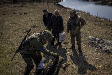 Ukrainian soldiers recover the charred foot of a dead Russian soldier as two local men look on, at a frontline position in the northern region of Kyiv.