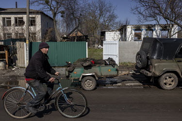 A man rides a bicycle past a trailer that contained the remains of 10 Russian soldiers collected from various points around the recently liberated village of Nova Basan. The soldiers had been killed w...