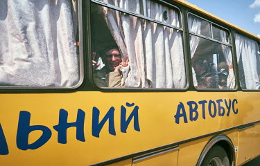 An elderly man looks out of a bus window and smiles as he flees to safety from war.