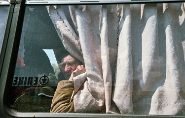 An elderly man looks out of a bus window as he flees to safety from war.