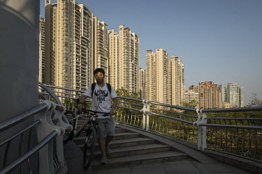 A cyclist walks down a flight of stairs, with his bicycle, from the Liede Bridge over the Pearl River. Rising behind is a huge residential tower block estate.