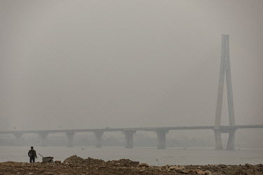 A man stands on the banks of Yangtze River where a thick haze shrouds the Tianxingzhou Yangtze River Bridge.