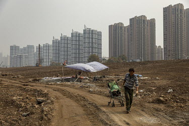 A man walks through a tract of development land near rows of newly built high rise housing blocks.