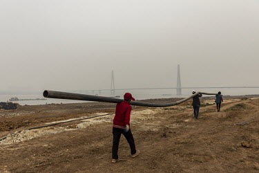 A crew of workers shoulder a long pipe as they walk on the bank of Yangtze River which is shrouded in heavy haze.