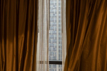 A view of an apartment building from behind a hotel curtain.