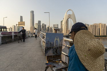 A man paints a cityscape while sitting on the Liede Bridge, which crosses the Pearl River.