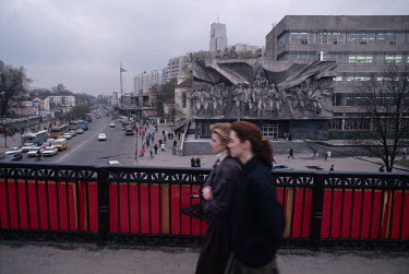 Women walk on a bridge past the House of Fashion, a Soviet-Brutalist style building with the relief 'Solidarity' by sculptor Anatol' Yafimovich Arcimovich.