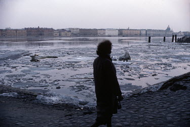 A woman walks past the Neva River as the ice coving its surface melts during the spring thaw.