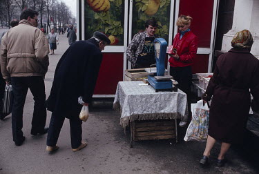 People buying fruit and vegetables from a pavement stall.