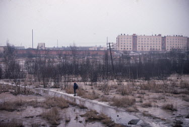 A youth stands in a n area of scrubland seen through the window of a train travelling from Helsinki to Leningrad.