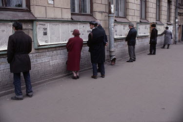 People reading a two day old state newspapers displayed on a wall in the streets for public information.