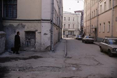A man stands on a decrepit side street.