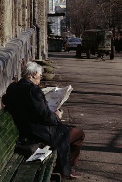A man reading a newspaper on the street near an abandonned portable generator.
