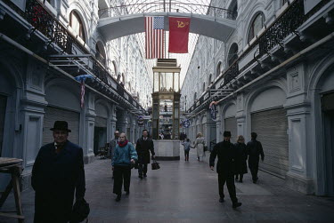People walk through a Government GUM department store, displaying both Soviet and American flags, although the shops are mostly closed.