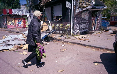 A woman carrying a bunch of lilacs passing Mr. Shawarma, a fast food shop destroyed on the evening of 7 May 2022 when four Russian missiles hit the market.