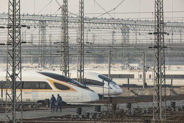 Railway employees walk past China Railway High-speed (CRH) trains, operated by China Railway Corp., sitting in a train yard on the outskirts of Shanghai.