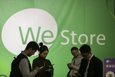 Attendees look at their smartphones in front of a WeStore sign at the WeChat Open Class Pro conference.
