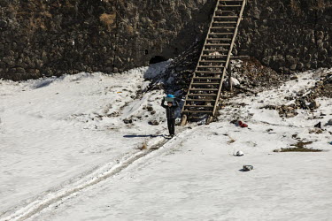 A woman carries a bucket of laundry towards a hole broken through the frozen surface of the Yalu River in Hyesan, North Korea, seen from across the border in Changbai.