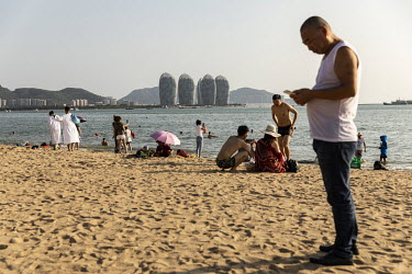 Tourists and residents play on a beach with a view of Phoenix Island, an artificial archipelago developed by Sanya Phoenix Island Development Co., in the background.