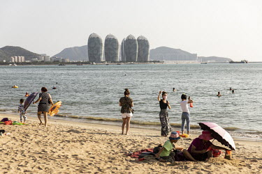 Tourists and residents play on a beach with a view of Phoenix Island, an artificial archipelago developed by Sanya Phoenix Island Development Co., in the background.