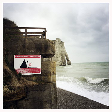 The remnants of a German WW2 concrete beach defence emplacement with the Etretat chalk cliffs and a sea arch beyond.