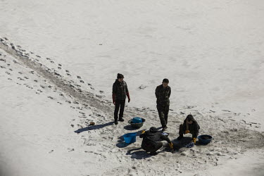 A soldier, stands and looks on as women wash clothes through a hole broken through the frozen surface of the Yalu River in Hyesan, North Korea, seen from across the border in Changbai.