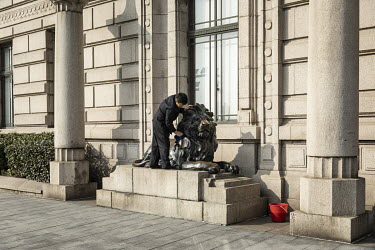 A man wipes down a lion statue in front of a bank on the Bund.