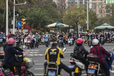 Motor scooterists wait at a traffic signal.