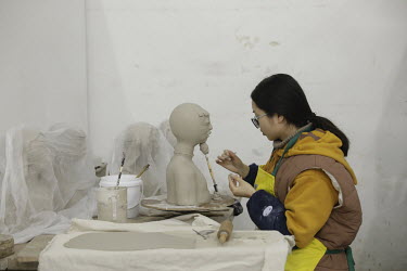 A crafts person working on a clay bust inside a workshop at the Jingdezhen Porcelain Factory.