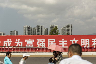 Tourists walk past a propaganda banner.
