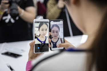 An attendee compares the beauty camera functions of a Xiaomi and an Apple smartphone at an unveiling event. Xiaomi Inc., is a Chinese designer and manufacturer of consumer electronics and related soft...