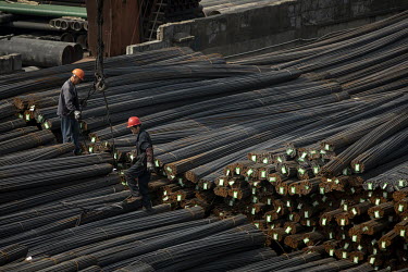 Workers stand on piles of steel rebars at a depot on the outskirts of Shanghai.