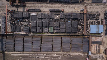 Piles of steel rods and steel wire sit in a depot and in barges moored beside it.