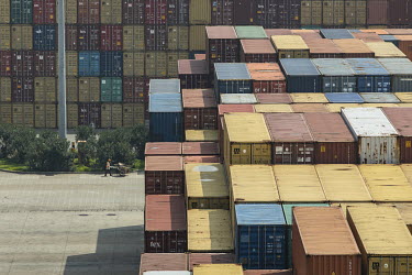 A worker pushes a cart past stacks of shipping containers stacked in a terminal at the Yangshan Deep Water Port.