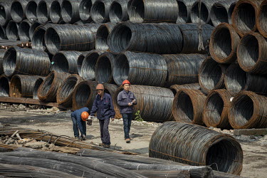 Workers walk past coils of steel wire at a depot on the outskirts of Shanghai.