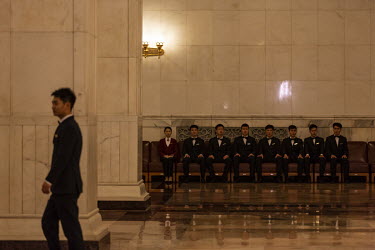 An attendant walks through the Great Hall of the People as others are seated in a row before the opening of the first session of the 13th National People's Congress (NPC).