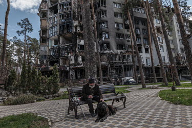 Valera with his dog Bars sitting in a small park near a destroyed apartment building. They lived through the bombardment of the town and their building was mostly destroyed. Valera said that Bars is n...