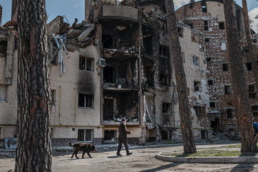 Valera with his dog Bars walking in a small park near a destroyed apartment building. They lived through the bombardment of the town and their building was mostly destroyed. Valera said that Bars is n...