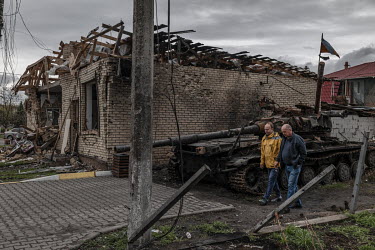 Two men walk past a destroyed tank in which five Ukranian soldiers died when it was hit by a drone attack.
